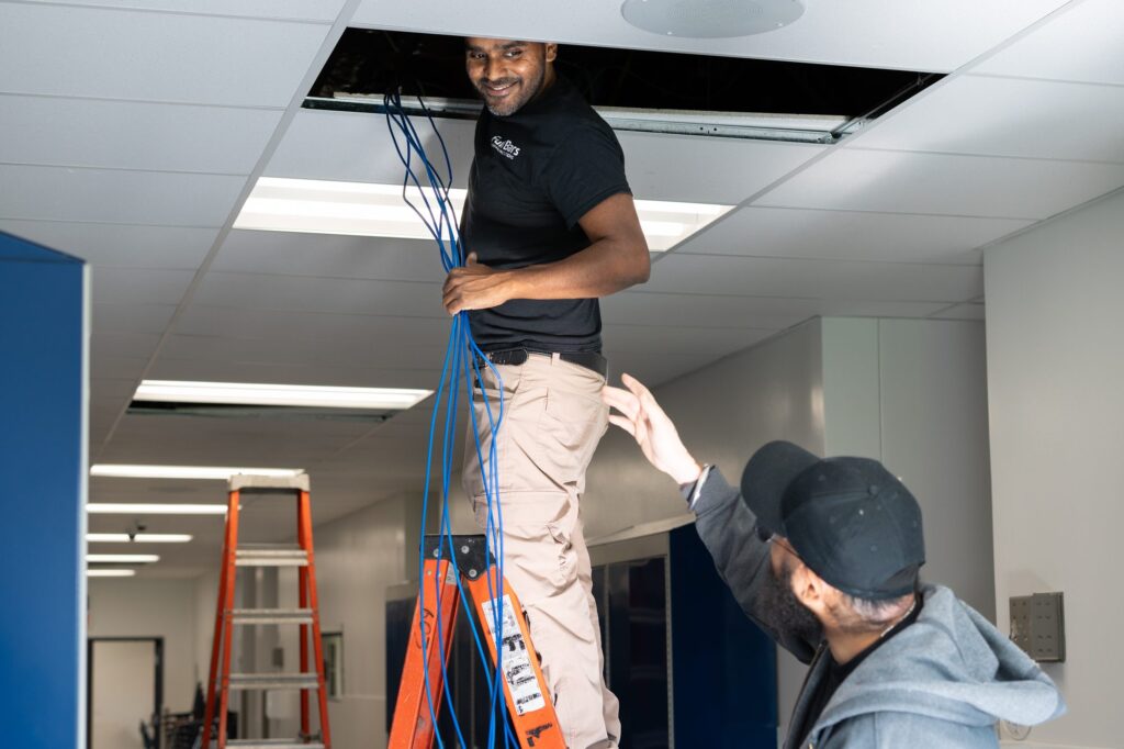 Full Bars technician pulling network cabling through a ceiling on a commercial jobsite while a second technician assists